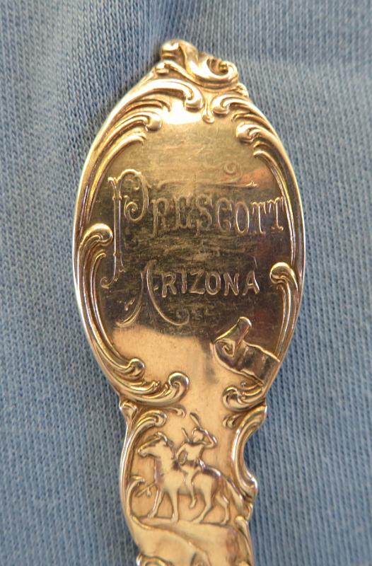 Souvenir Mining Spoon Prescott AZ Handle Reverse.JPG - SOUVENIR MINING SPOON PRESCOTT AZ - Sterling silver souvenir spoon, features handle with miner and gold rocker box at top above picks and ore bucket, bowl embossed in deep relief with miner single jacking with artist marking H. OTTO in small letters near tip, back of handle marked PRESCOTT,ARIZONA at top above figure of cowboy on horse, back marked STERLING with makers mark of George E. Homer (Boston, MA 1875 - ?) and COPYRIGHTED, measures 5 1/2 in. length , weighs 37.3 gr. [Prescott is located in the Bradshaw Mountains of central Arizona, approximately 100 miles north of Phoenix.  The new town of Prescott was named in honor of historian William H. Prescott during a public meeting in 1864 and was officially incorporated in 1881. Prescott twice served as the capital of the Arizona Territory, once till November 1867 and again from 1877 to 1889 when the capital was moved to Phoenix.   Gold was discovered in creeks in the Agua Fria River Basin near Prescott in 1863.  Joseph Walker and a party of prospectors had set out from the California gold fields, possibly fleeing from conscription in the Confederate or the Union Army during the Civil War.  They found gold placers and, shortly afterward, lode deposits.  These discoveries were in what collectively became the Big Bug Mining District a few miles southeast of Prescott.  When the railroad arrived around 1898 transportation of equipment, minerals, and people became easier and cheaper.  Gold, silver, lead, and/or copper were produced from several famous mines including the Poland, McCabe, Silver Belt, Little Jessie, Henrietta/Big Bug, Blue Bell, Boggs/Iron Queen, and Iron King.  Several smelters were also built in the area.  The World War I era saw the greatest production from the district; however, the post-war drop in metal prices caused many mines to close.  The Iron King was the last of the major mines in the district.  After a series of different owners, it was operated by the Shattuck-Denn Mining Company from 1942 until it closed in 1969.  Prospectors staked claims in the Jerome District approximately 35 miles northeast of Prescott in 1876.  In 1882 the United Verde Copper Company was formed and mining started.  The rich oxidized ores produced copper, gold, and silver.  Transportation costs were very high until William A. Clark of Butte, Montana fame bought the company and brought the railroad to Jerome.  The United Verde Mine prospered and became the largest copper mine in the territory.  The original smelter built on unstable ground adjacent to the mine was replaced by a larger, more efficient one in Clarkdale.   In 1912, the Little Daisy Mine near the United Verde was purchased by James S. Douglas.  In 1914 and 1916 rich ore bodies were discovered.  A smelter was built in Clemenceau near the current town of Cottonwood.  The United Verde Extension Mining Company mined out the extension in 1930.  Phelps-Dodge purchased the United Verde and operated an open pit until mining ceased in 1953.  Today, the Douglas Mansion adjacent to the Little Daisy Shaft is part of the Jerome State Historic Park.  Jerome was designated a National Historic District in 1967.  Many of the historic buildings in Jerome have been converted to shops and eateries catering to tourists.  The Jerome Historical Society Museum occupies one of the buildings.  The Bagdad Mining District is located about 40 miles west of Prescott.  It has a rich history of mining including such famous mines as the Old Dick, Copper King, Copper Queen, and the Hillside among others.  The Bagdad deposit was discovered in 1862 and the claims were patented in 1889.  It was owned by a series of companies.  Exploration drilling was started in 1919 and the first mill was constructed in 1928.  During World War II, a 2000 ton per day mill was constructed with funds from the Reconstruction Finance Corporation. In the late 1940’s, the underground mine using block caving was converted to an open pit.  The town of Bagdad was a company town.  In 1973 the Bagdad Copper Corp. merged with the Cyprus Mines Corp. to form the Cyprus Bagdad Copper Company.  It later became part of Phelps-Dodge.  As a result of the 2007 merger, the mine is now operated by Freeport-McMoRan Copper and Gold Corporation. ] 